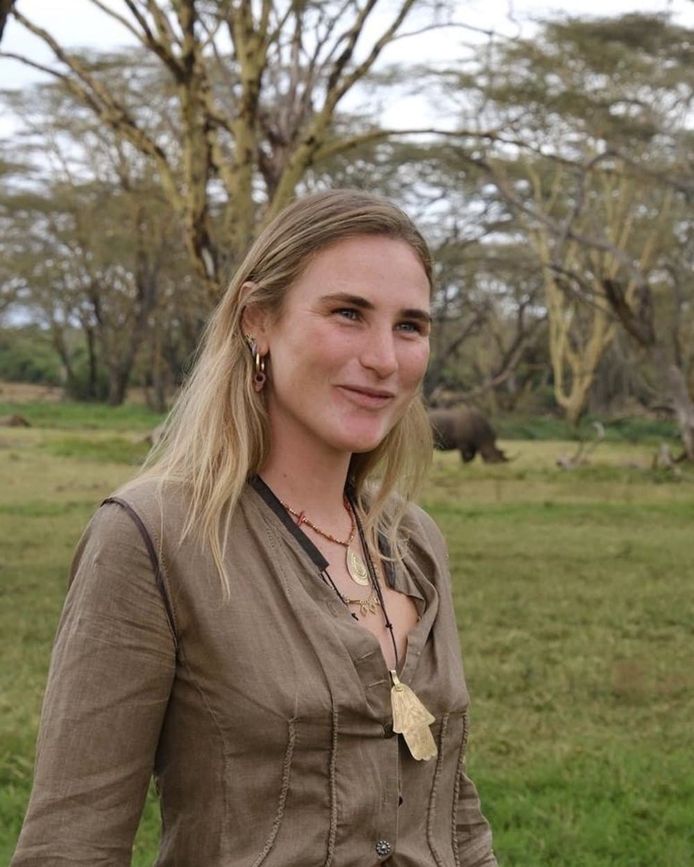 Cassia-Peia among fever trees, with a rhino grazing behind her